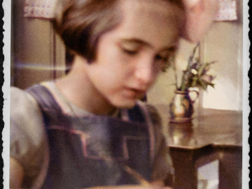 Op de foto Edith zittend aan tafel, ze is aan het schrijven.