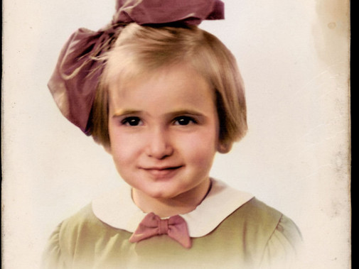 Portretfoto van Edith Beek in kleur: een jong meisje met een grote roze strik in haar haar. 