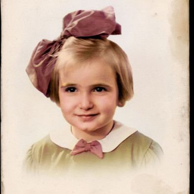 Portretfoto van Edith Beek in kleur: een jong meisje met een grote roze strik in haar haar. 