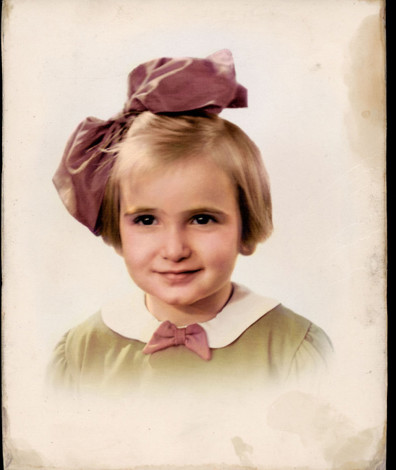 Portretfoto van Edith Beek in kleur: een jong meisje met een grote roze strik in haar haar. 