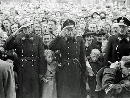 De geallieerden troepen op de Markt in Delft. Voor het Stadhuis salueerden agenten in uniform. En een fotograaf rechtsonder die hen fotografeerde. Op 8 mei 1945. Fotograaf: Tiemen van der Reijken.